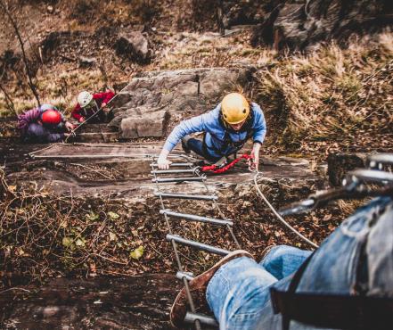 Bergklimmen Een groep mensen klimmen met een ladder een berg omhoog.